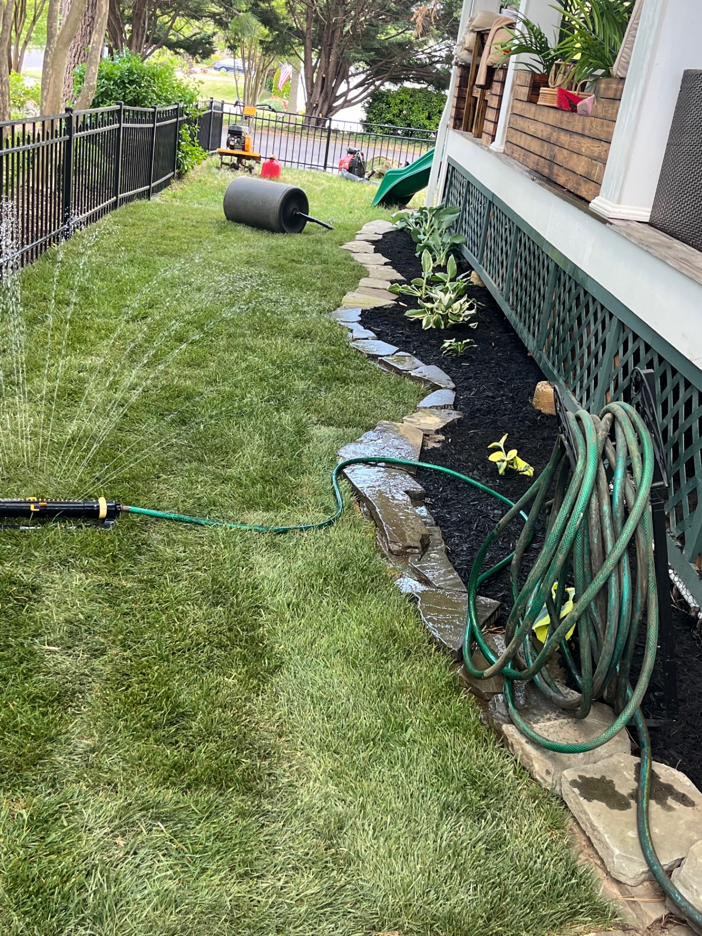 Freshly rolled lawn being watered beside a stone-edged bed